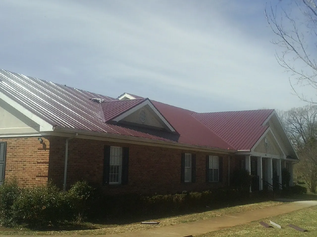 Red metal roof with gabled entries on a long brick building, from a Hail Damage Roof Repair job in Greeneville