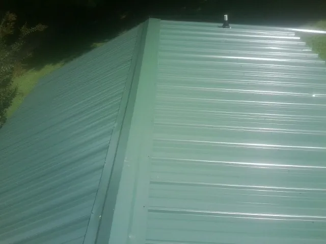 New green metal panels meeting at the ridge of a roof — Flat Roof Repair work by our crew in Greeneville