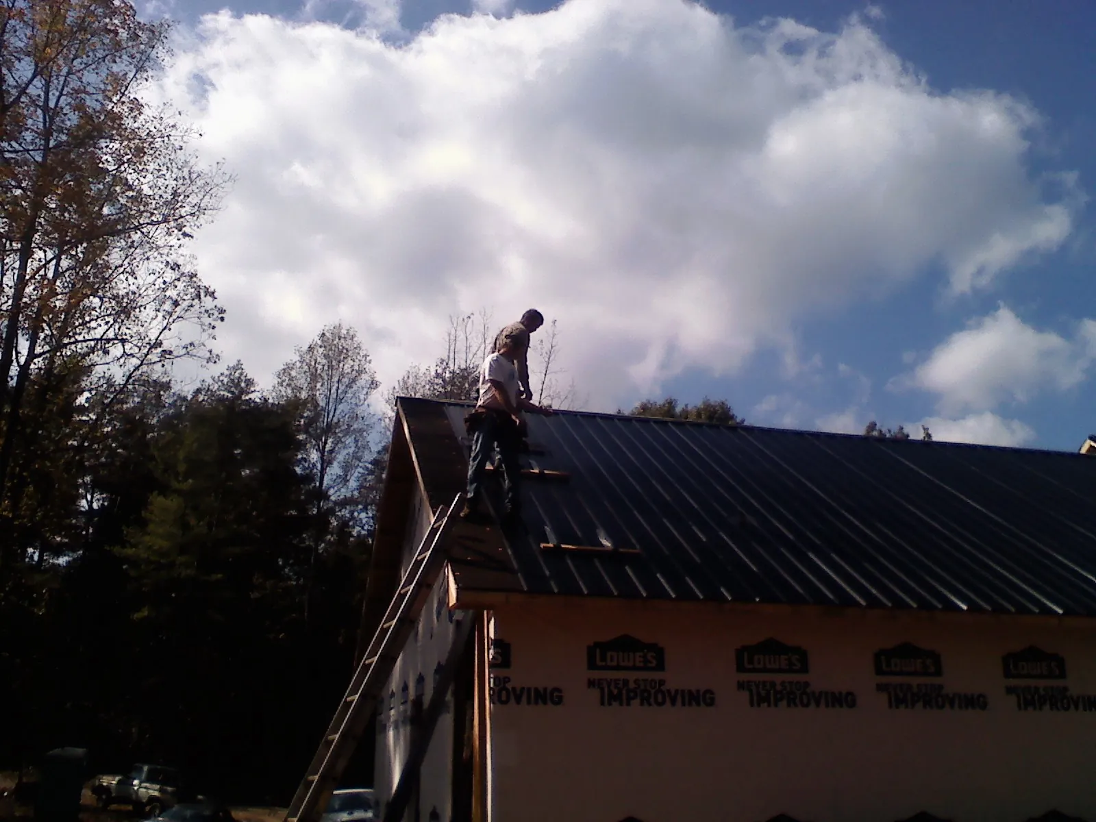 Roofer fastening dark metal panels high against a cloudy sky, from a Roof Inspection job in Greeneville