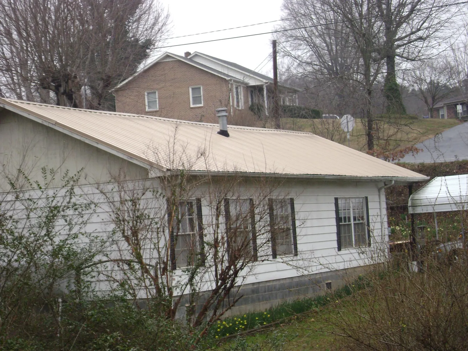 Tan metal roof on a white sided house set into a hillside — Commercial Roofing by Roofing Brothers in Greeneville